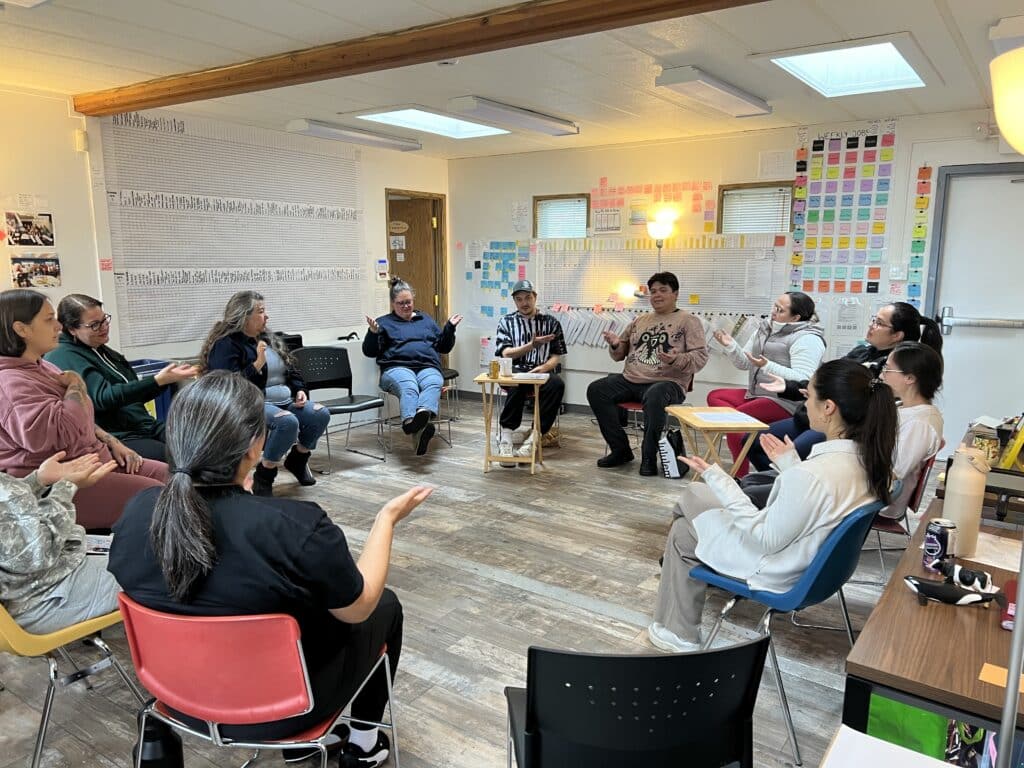 Staff and learners at the Treehouse Language Program at the Gwa'sala-Nakwaxada'xw Nations in Port Hardy, BC sit in a circle during an immersion language activity with the WAYK team.